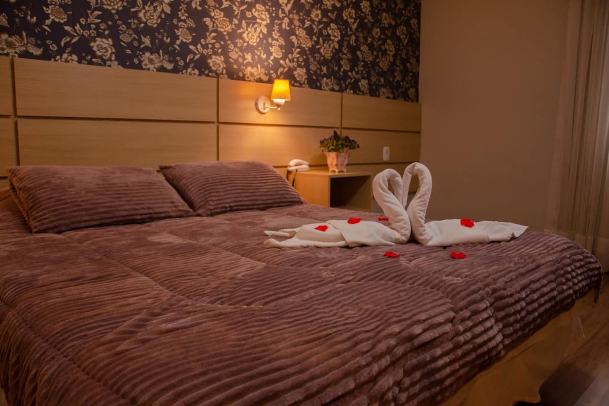 Hotellihuone, jossa on suuri sänky, yöpöytä, lamppu ja kukallinen tapetti.