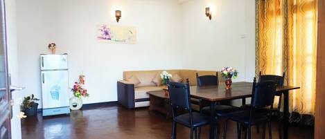 A dining area with a table, chairs, a refrigerator, a sofa, and wall-mounted lights.