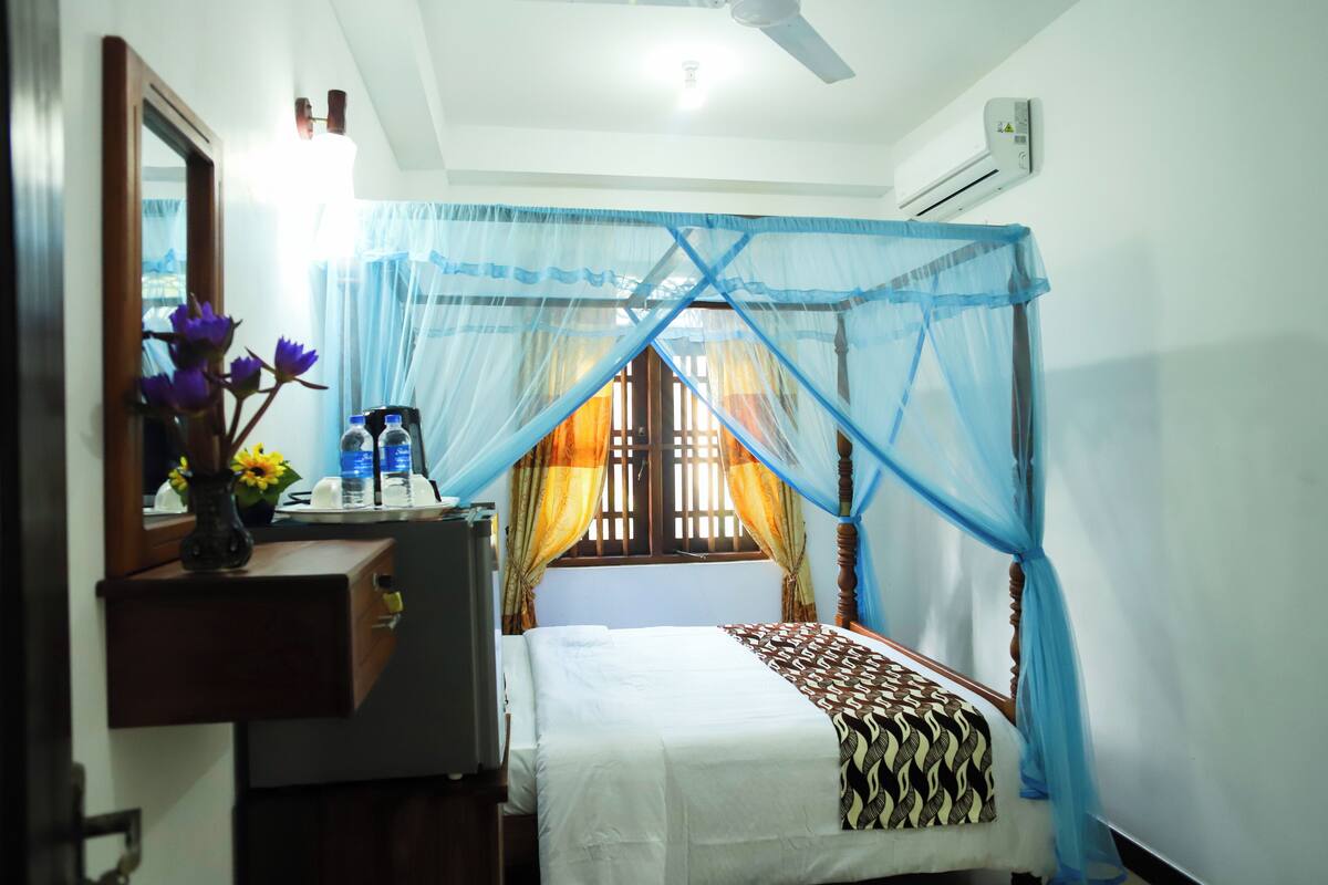 A bedroom with a bed, a nightstand, a mirror, and a window with curtains.