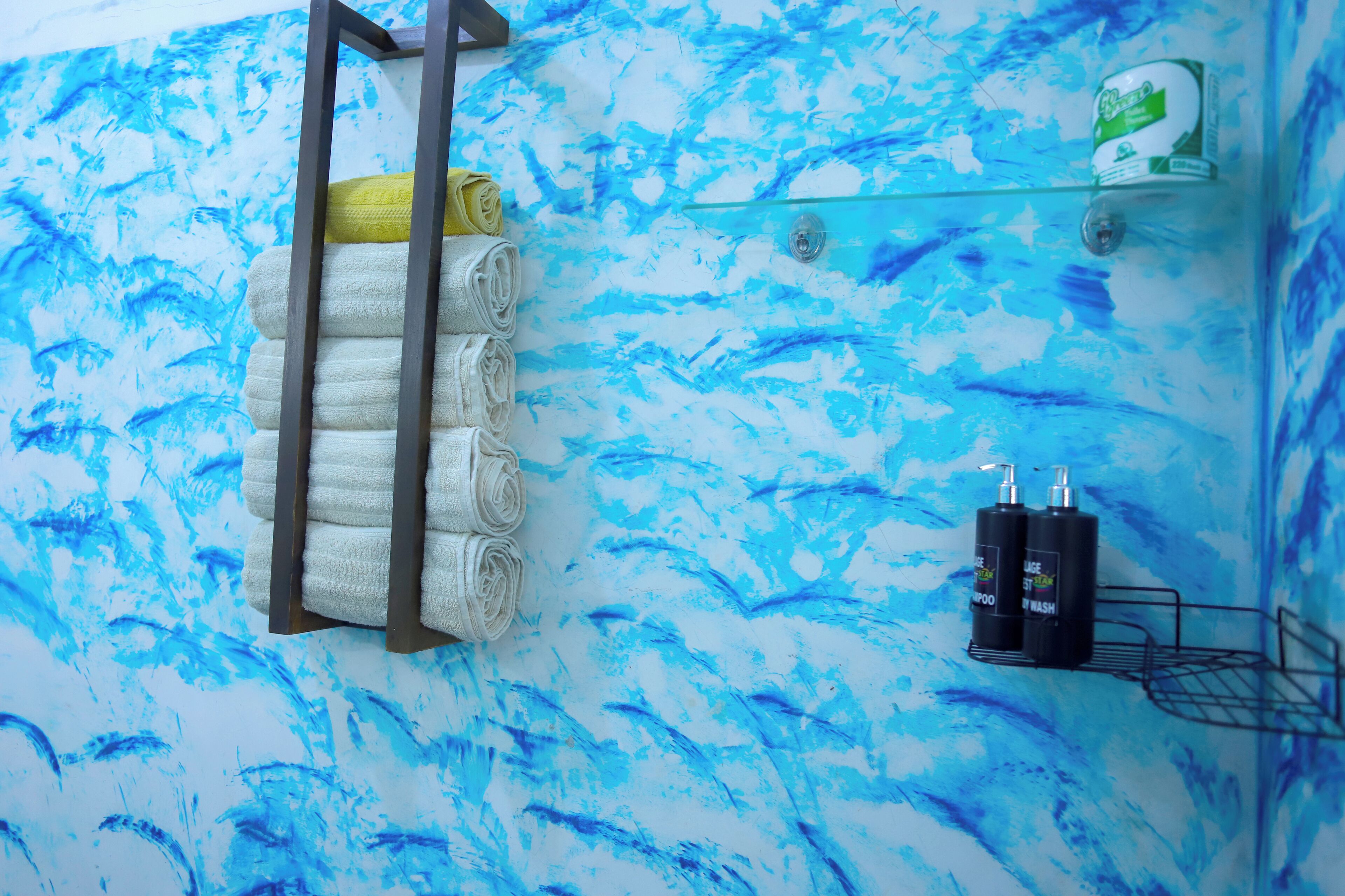 Un baño con un diseño abstracto azul en la pared, un perchero con toallas y un estante con artículos de aseo.