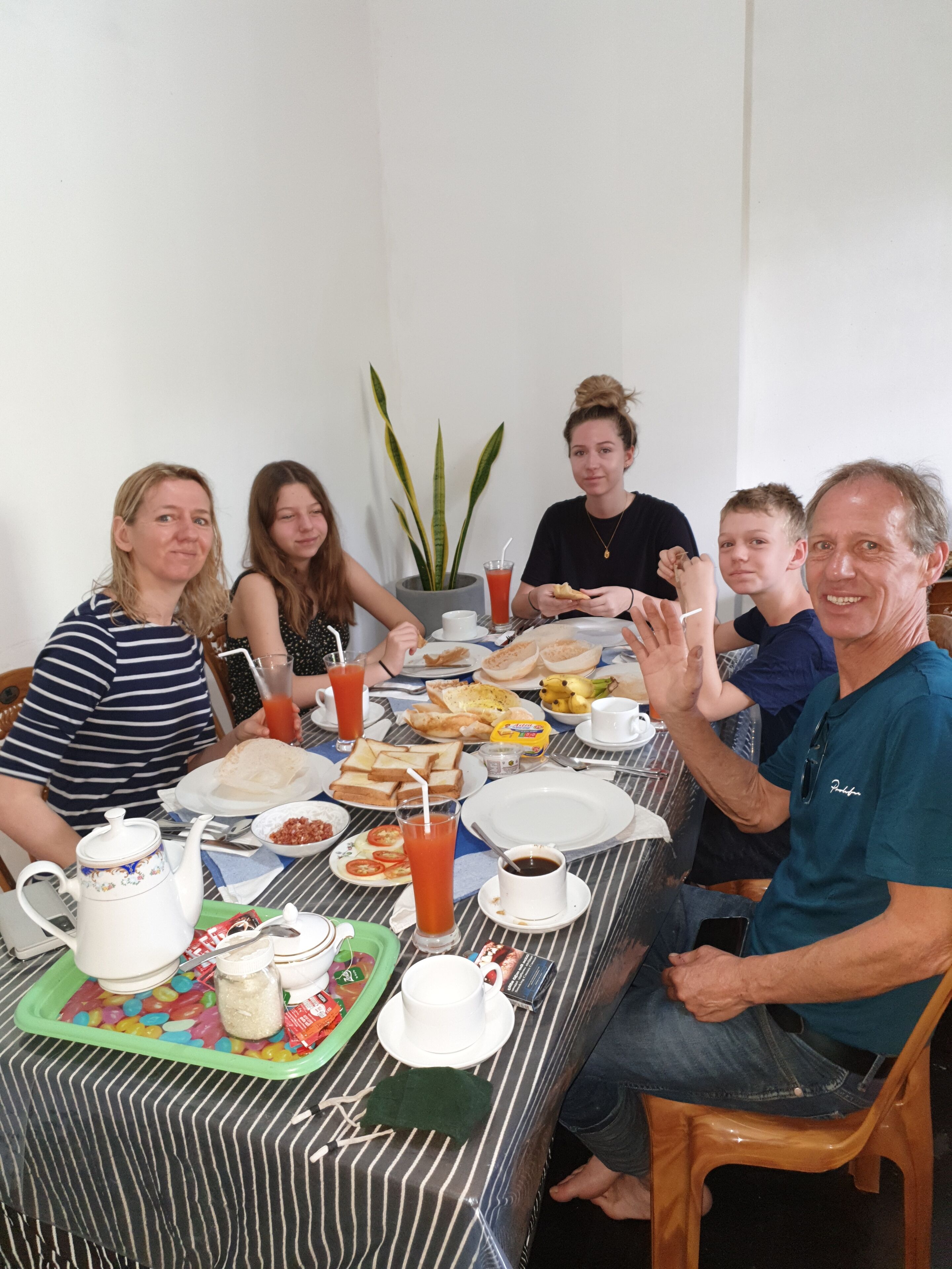 Une table à manger, dressée avec diff érents plats et boissons, autour de laquelle sont rassemblées des personnes.