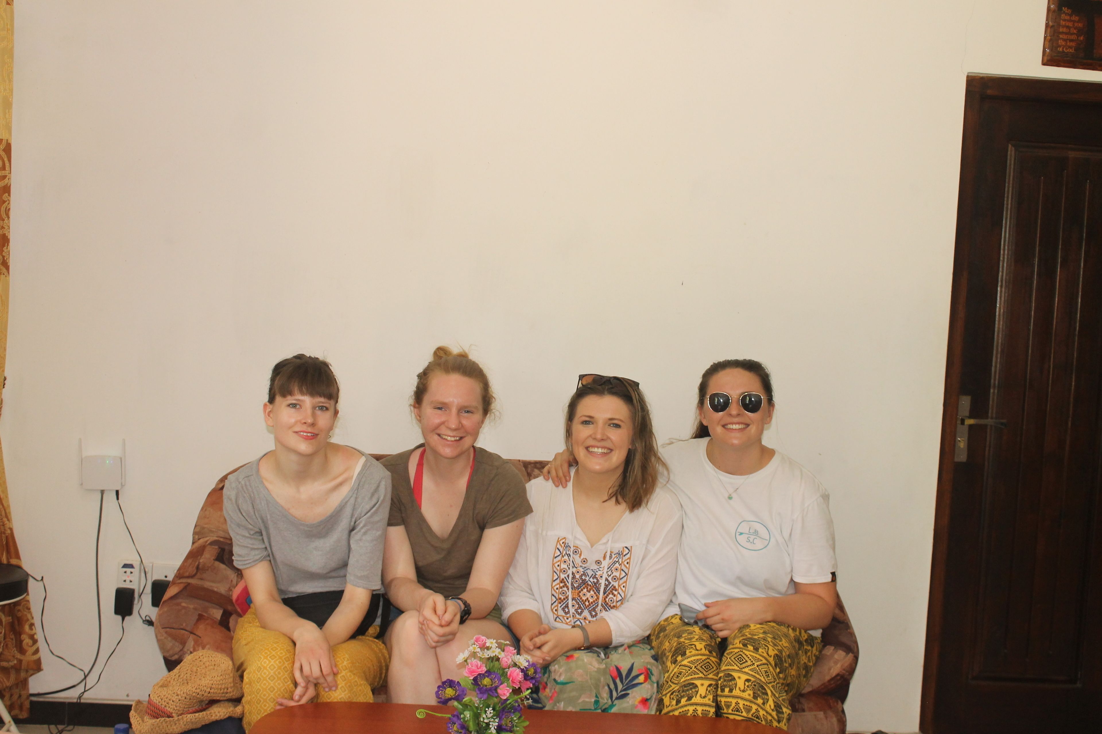 A group of four people sitting on a couch in a room with a plain wall and a wooden door.