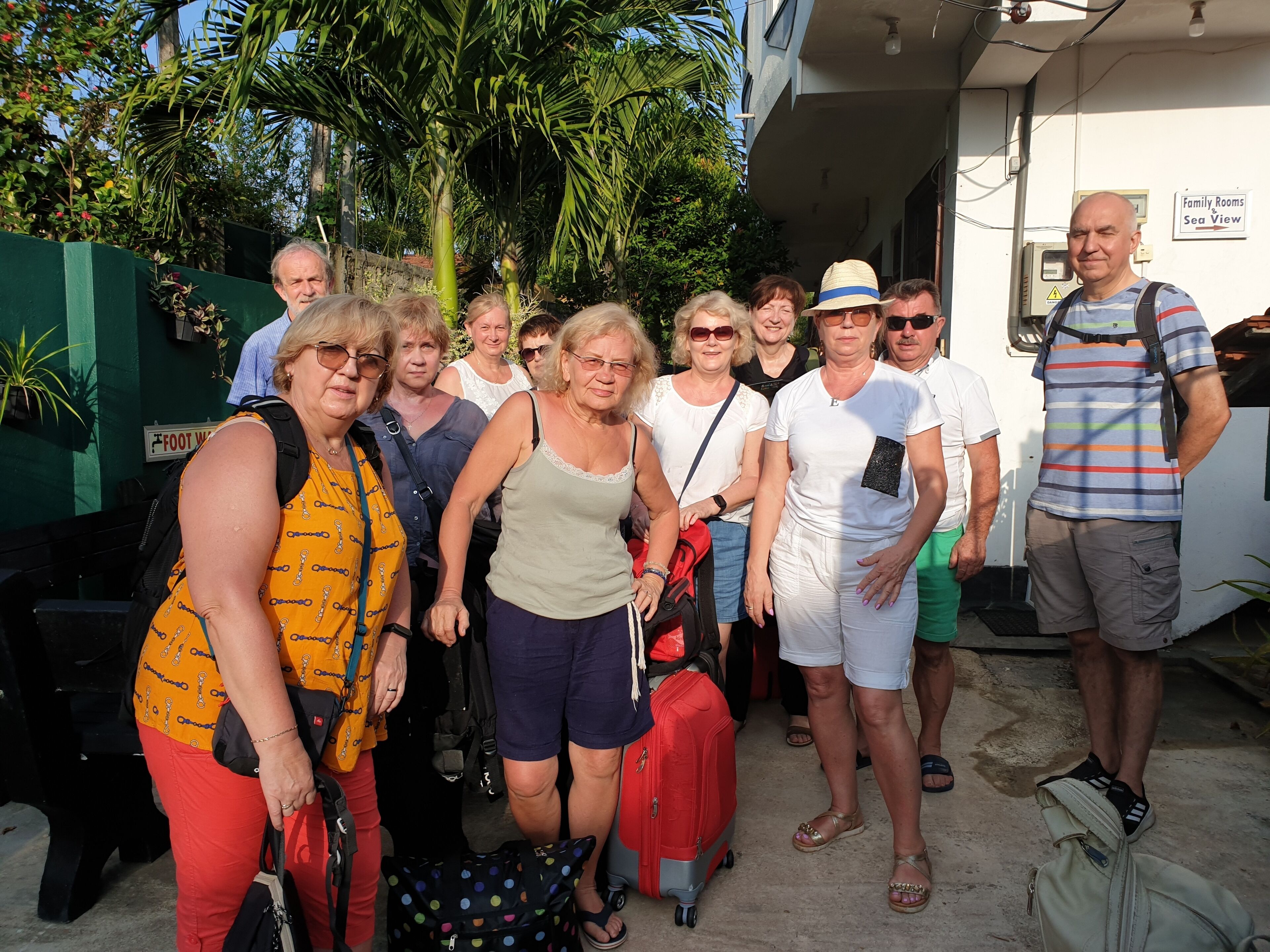 Un groupe de personnes se tient devant un bâtiment, et une pancarte indique : « Chambres familiales avec vue sur mer ».