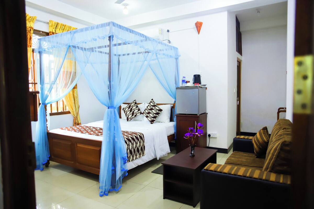A bedroom with a four-poster bed, a sofa, a small table, and a nightstand.