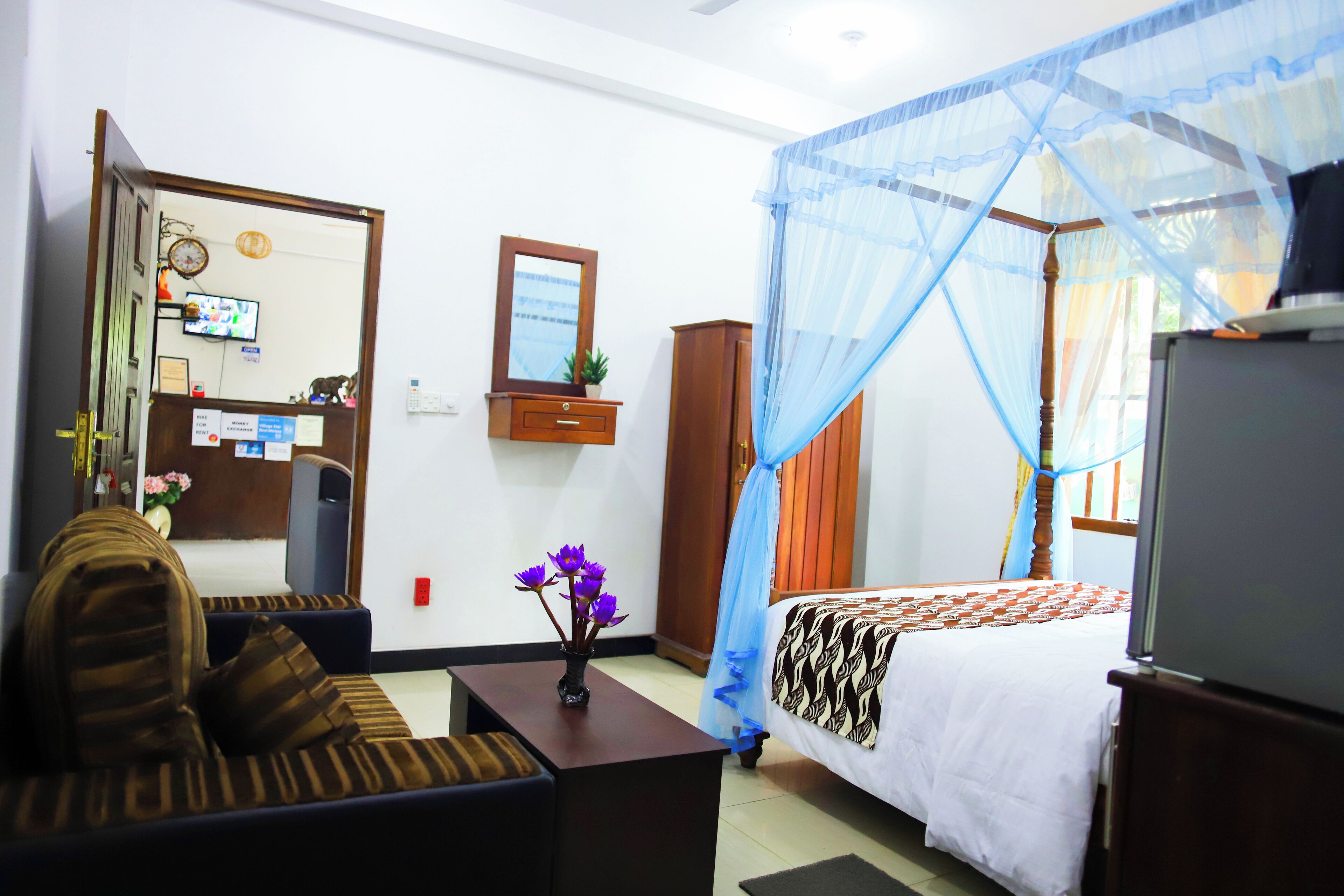 A hotel room with a bed, a sofa, a television, a desk, and a mosquito net.