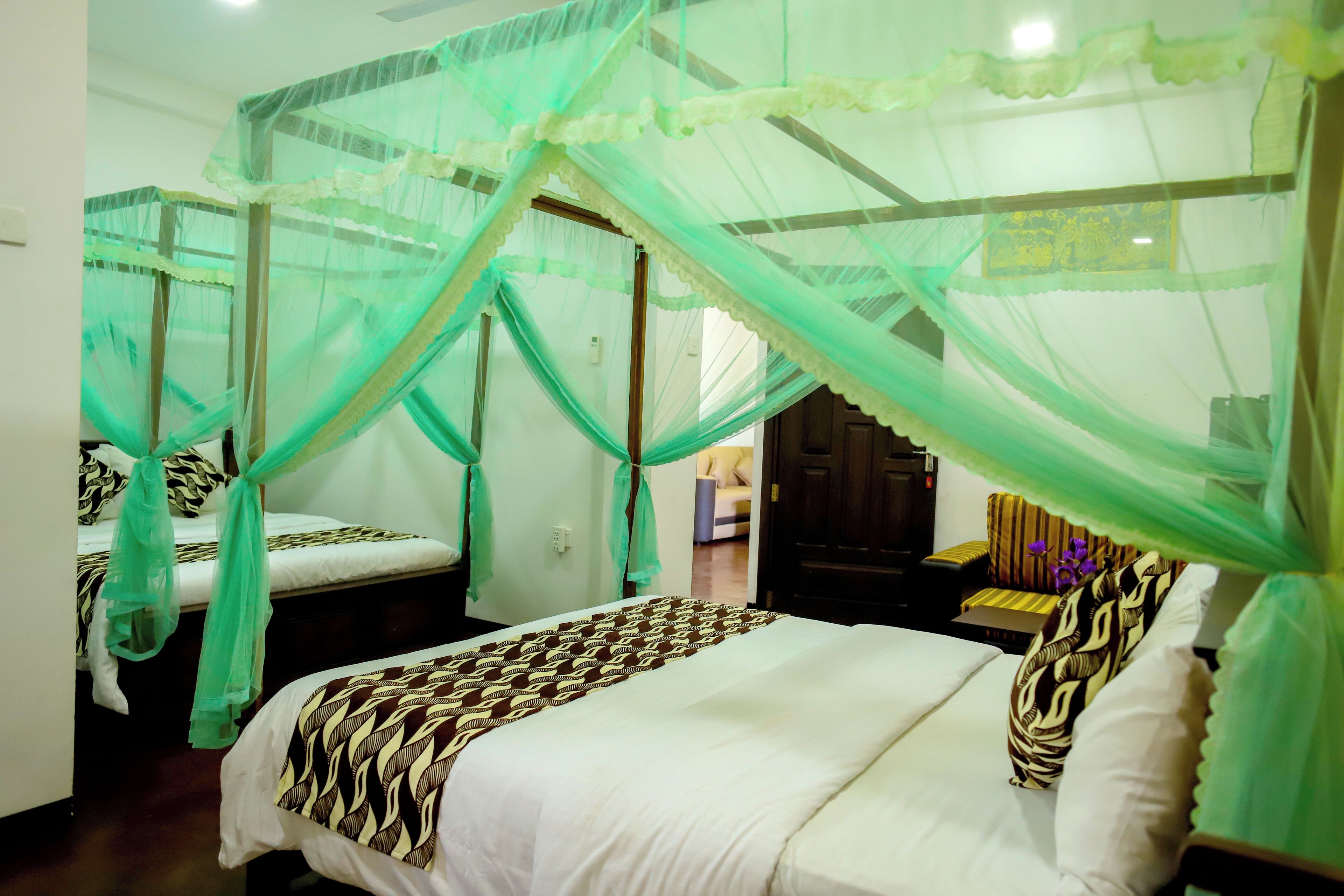 Una habitación con una cama cubierta por una mosquitera, una colcha estampada y una mesita de noche con una lámpara.