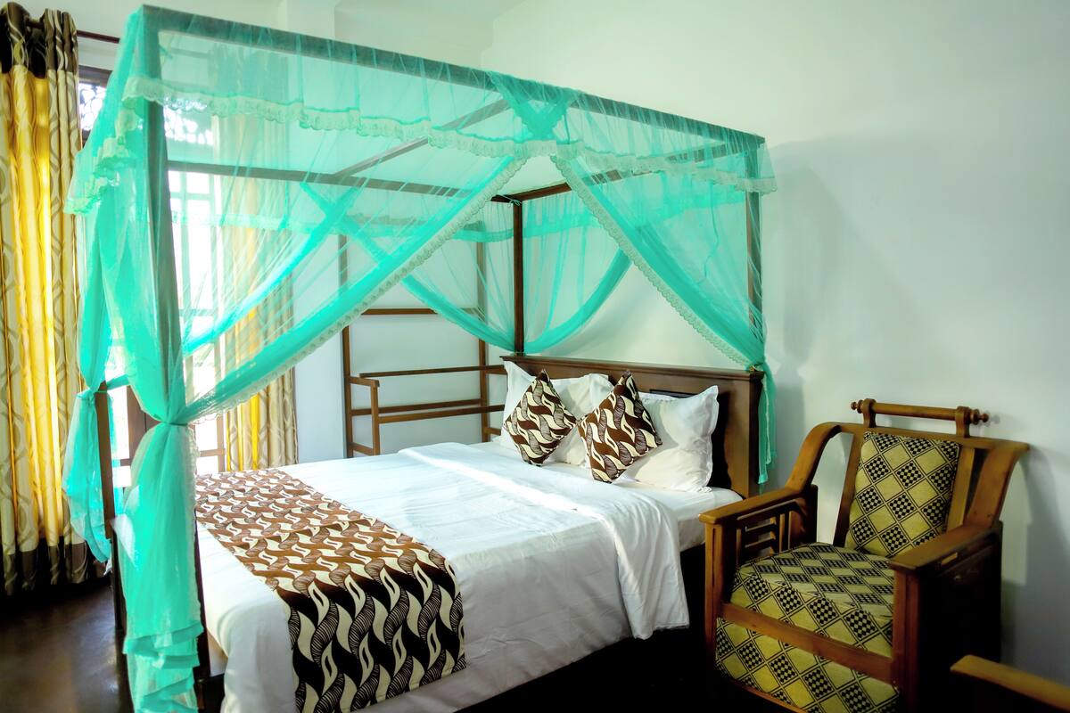 A bed with a mosquito net, a wooden chair, and a patterned pillow.