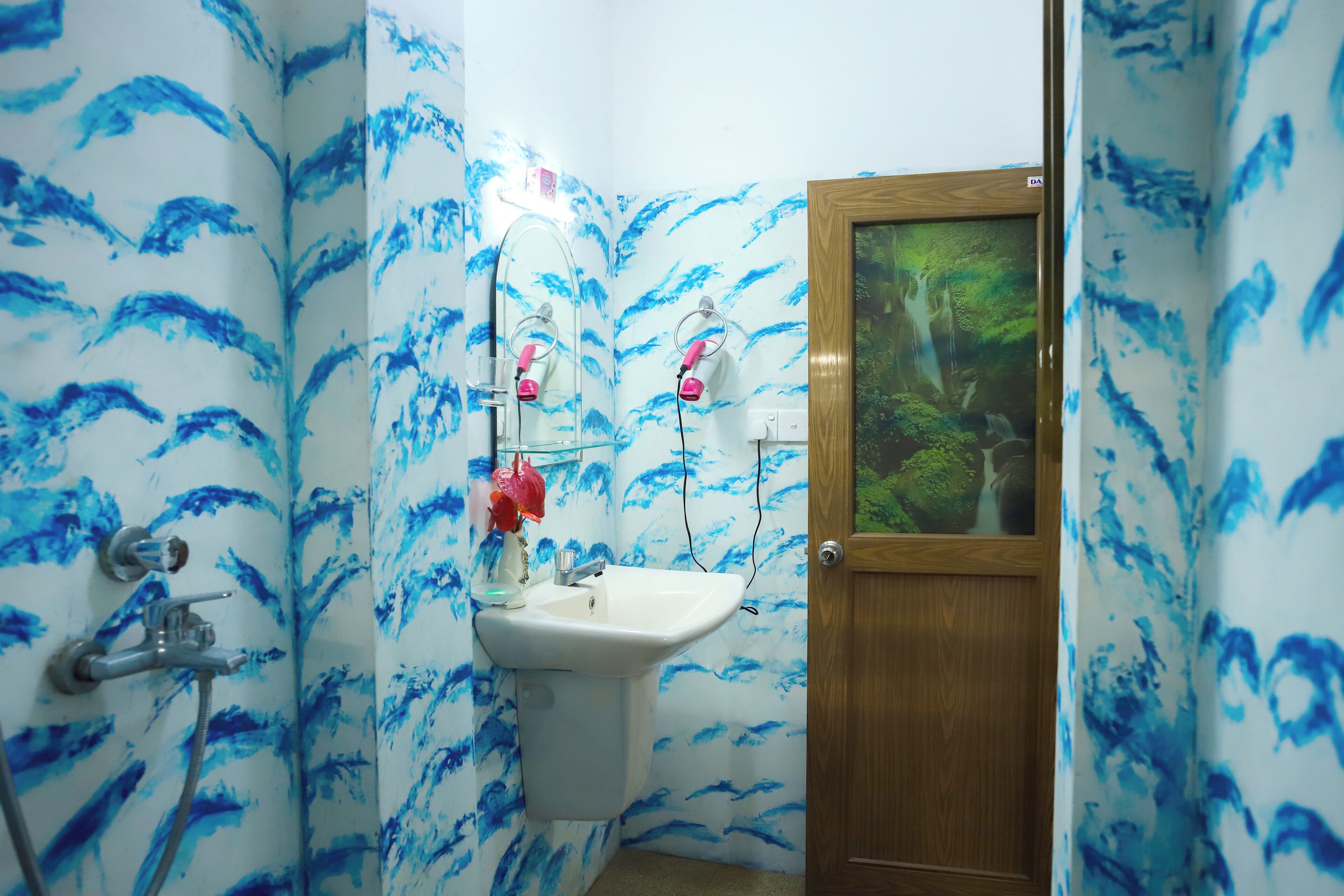 A bathroom with blue wave patterns on the walls, a wooden door, and a sink with a mirror.