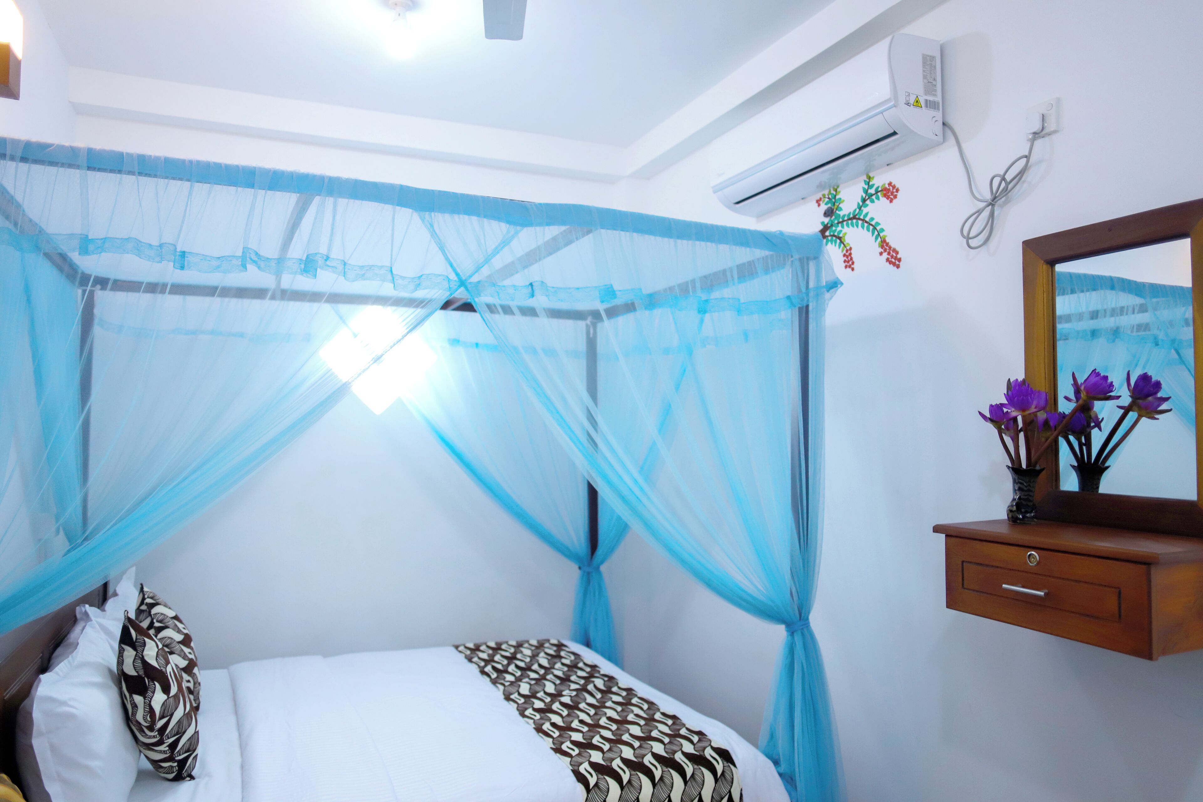 A bedroom with a bed, a bedside table with a vase of flowers, and a wall-mounted air conditioner.