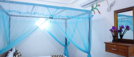 A bedroom with a bed, a bedside table with a vase of flowers, and a wall-mounted air conditioner.