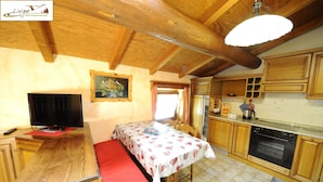 A cozy room with a bed, a television, a dining table, and a kitchen area. - Appartamento Valeriano (Livigno)