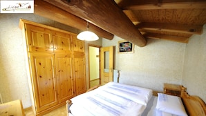 A wooden bedroom with a bed, a wardrobe, and a ceiling with exposed beams. - Appartamento Valeriano (Livigno)