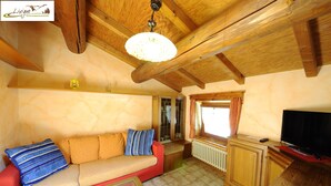 A cozy living room with a red sofa, a glass coffee table, wooden beams on the ceiling, a television, and a window with curtains. - Appartamento Valeriano (Livigno)