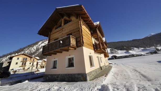 A wooden chalet with a balcony, set against a snowy mountain backdrop. - Appartamento Valeriano (Livigno)