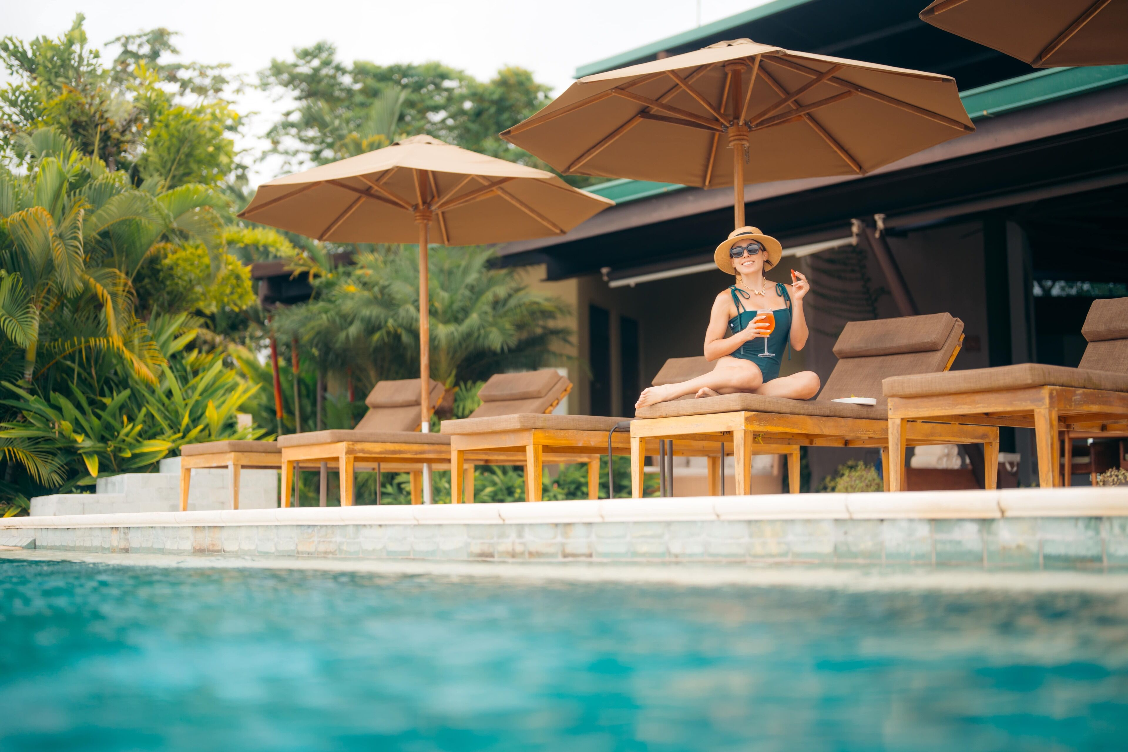 A poolside area with lounge chairs and umbrellas, surrounded by greenery.