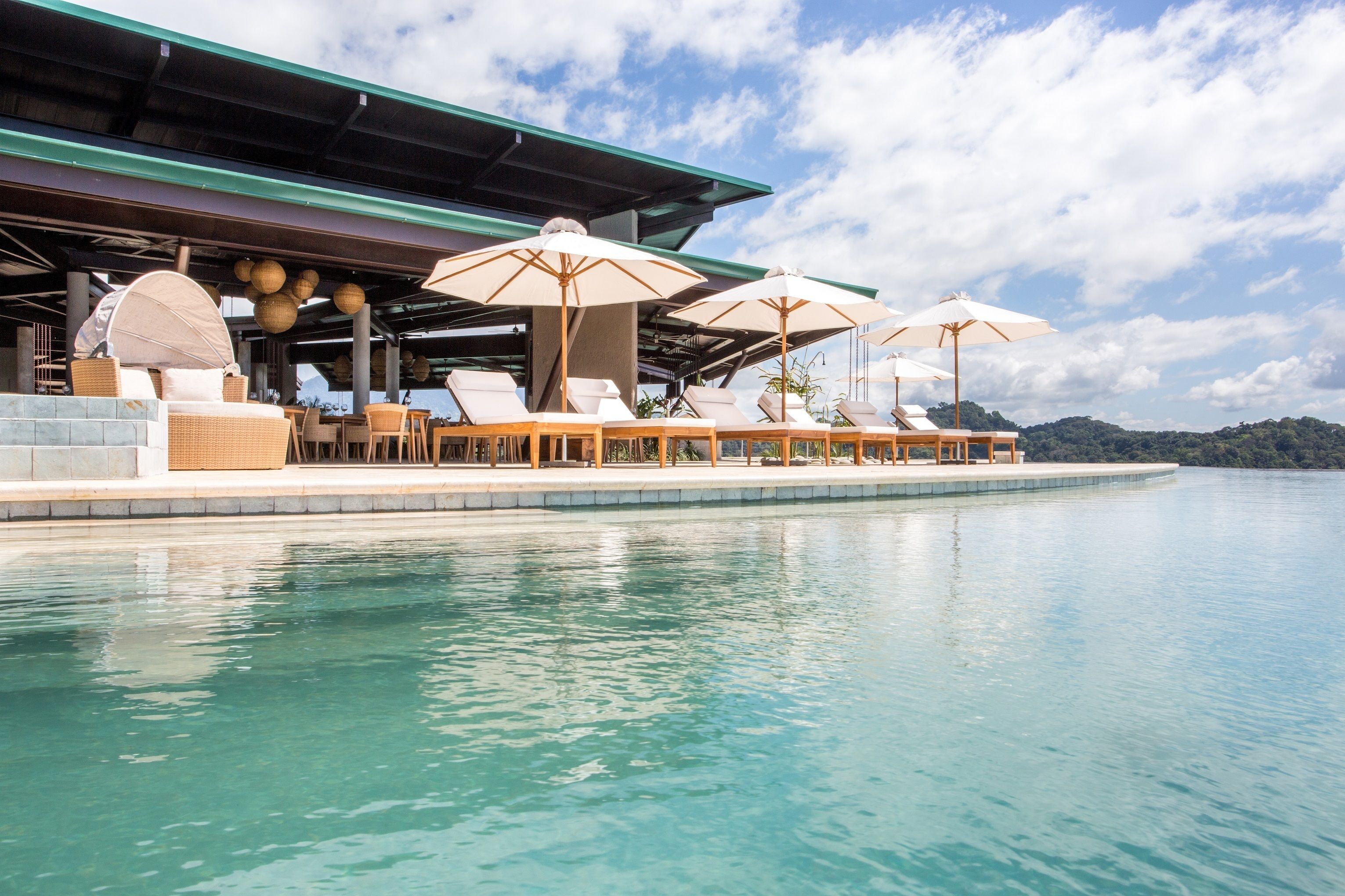 A poolside area with lounge chairs and umbrellas, a covered seating area, and a view of the water.