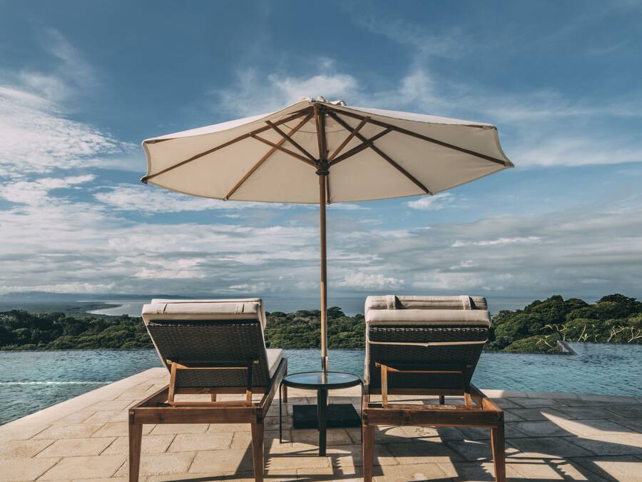 Two wicker lounge chairs with a table and an umbrella on a patio overlooking a body of water.