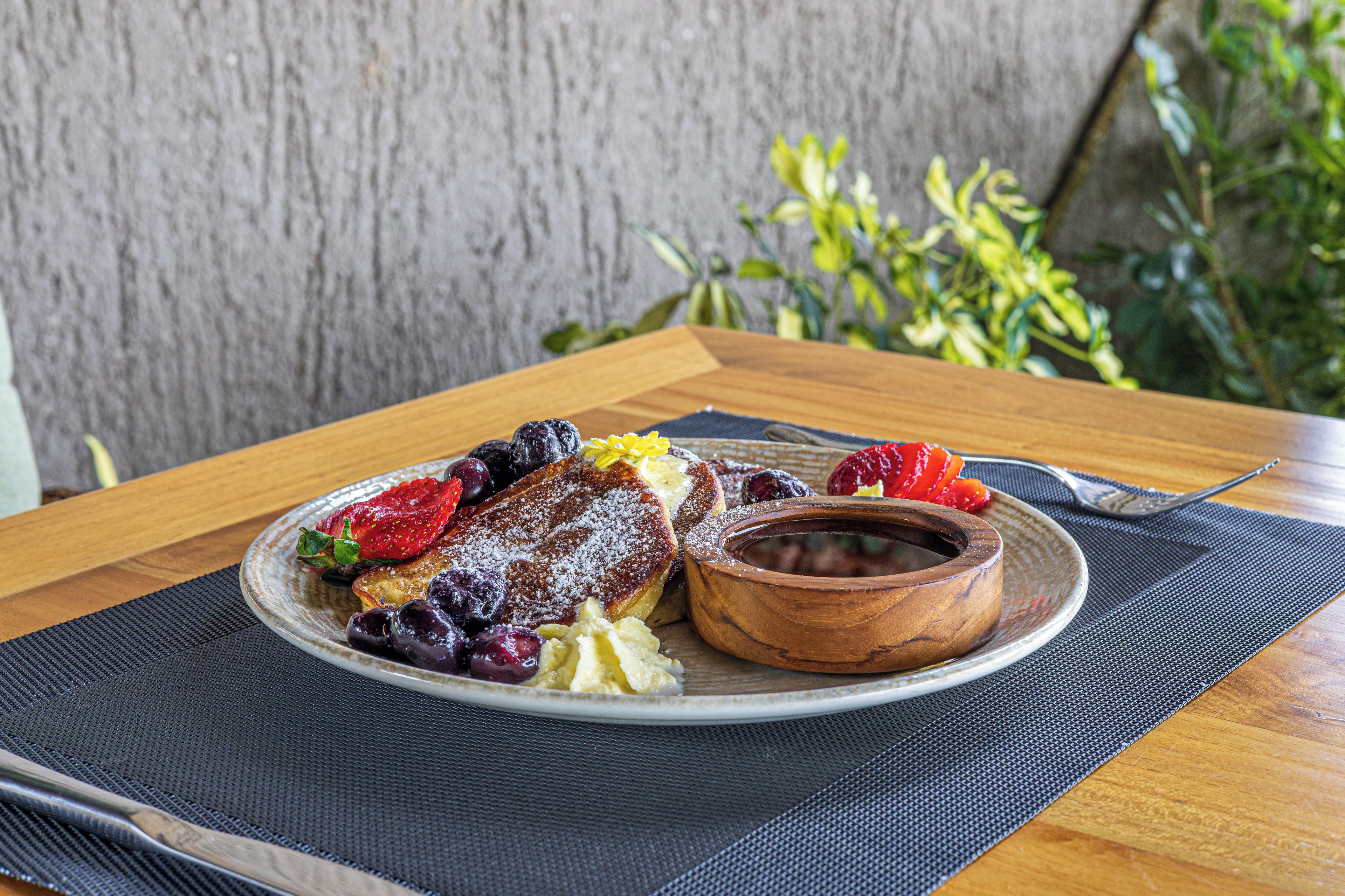 A breakfast plate with pancakes, berries, and a small bowl of jam on a table with a placemat.