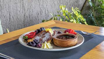 A breakfast plate with pancakes, berries, and a small bowl of jam on a table with a placemat.