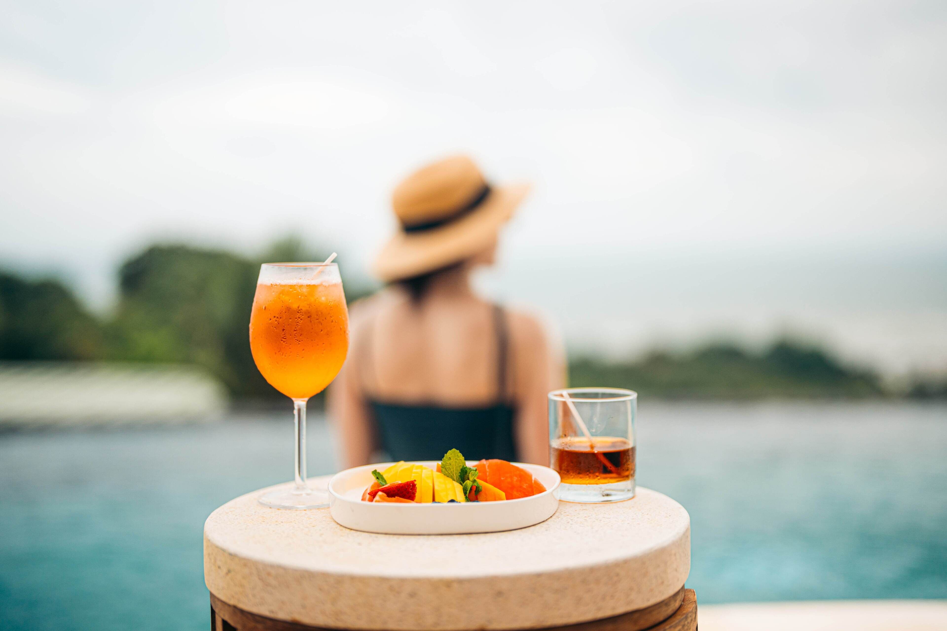 Une table avec un verre de boisson à l’orange, une assiette de fruits et une tasse de thé, donnant sur une étendue d’eau.