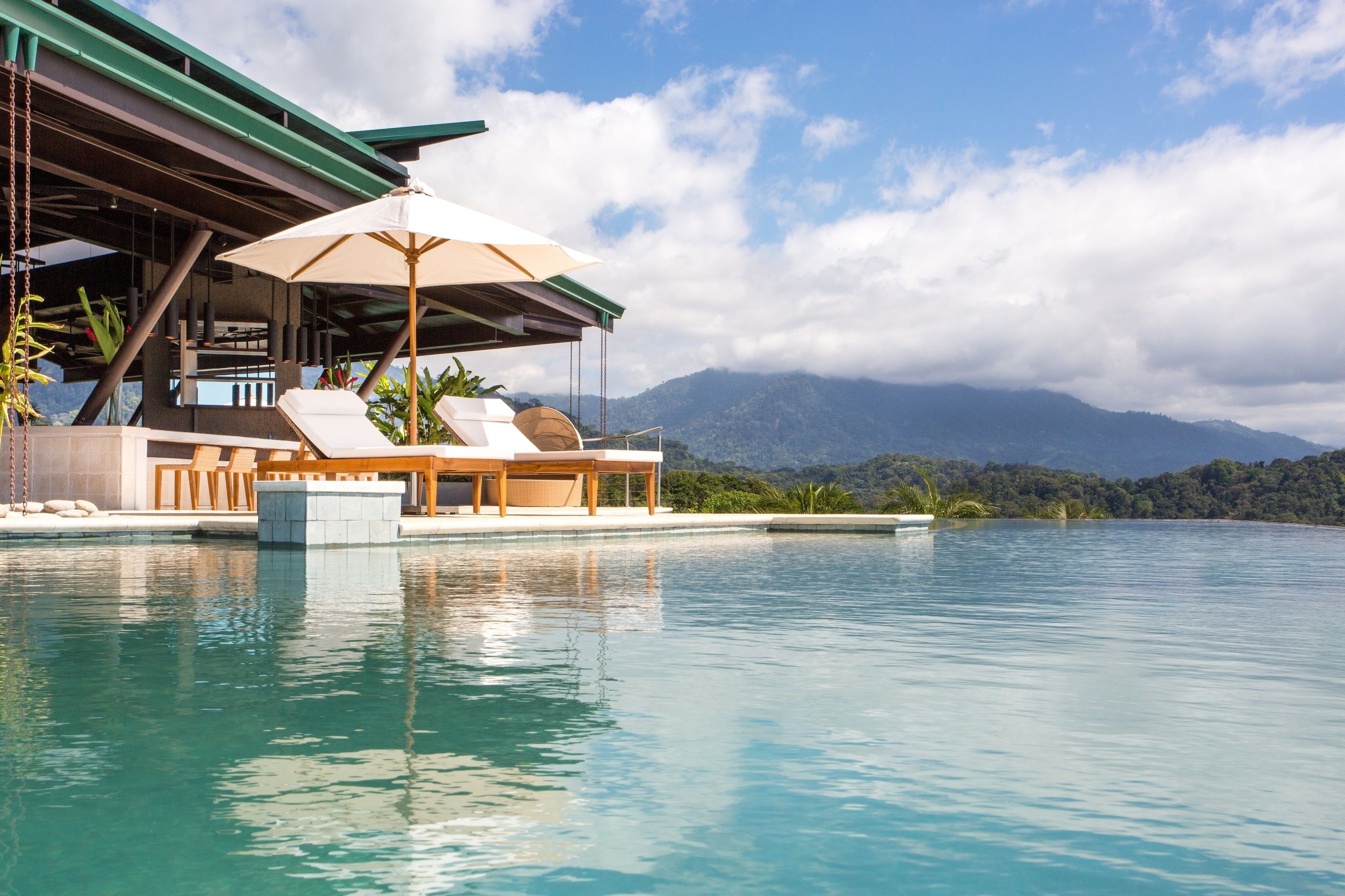 A pool area with lounge chairs and a covered seating area, overlooking a mountainous landscape.