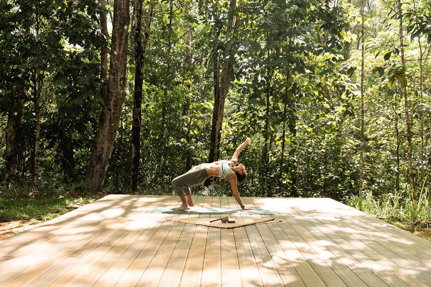 A person performing a yoga pose on a wooden deck surrounded by trees.