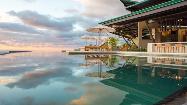 An infinity pool with lounge chairs and umbrellas, reflecting the sky and clouds. - Hotel Three Sixty - Adults Only (Ciudad Cortés)