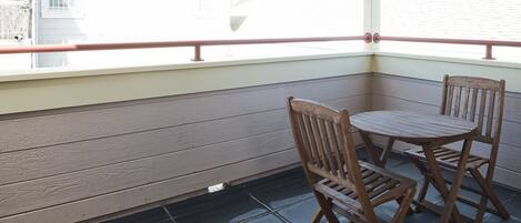 A corner of a room with a wooden bench and a table, a window with a view of the outside, and a railing along the window.