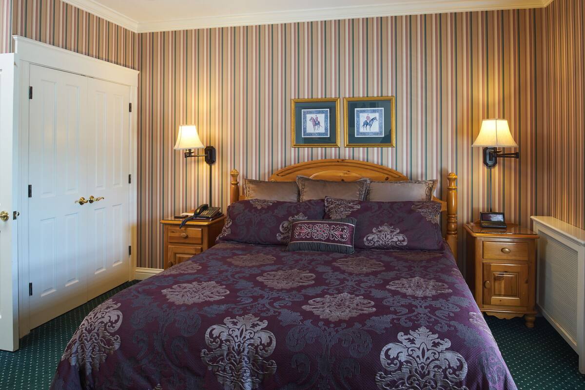 A hotel room with a large bed, two bedside tables, a wooden headboard, and striped wallpaper.