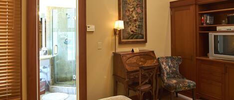 A hotel room with a bed, a wooden desk, a chair, a television, and a painting on the wall.