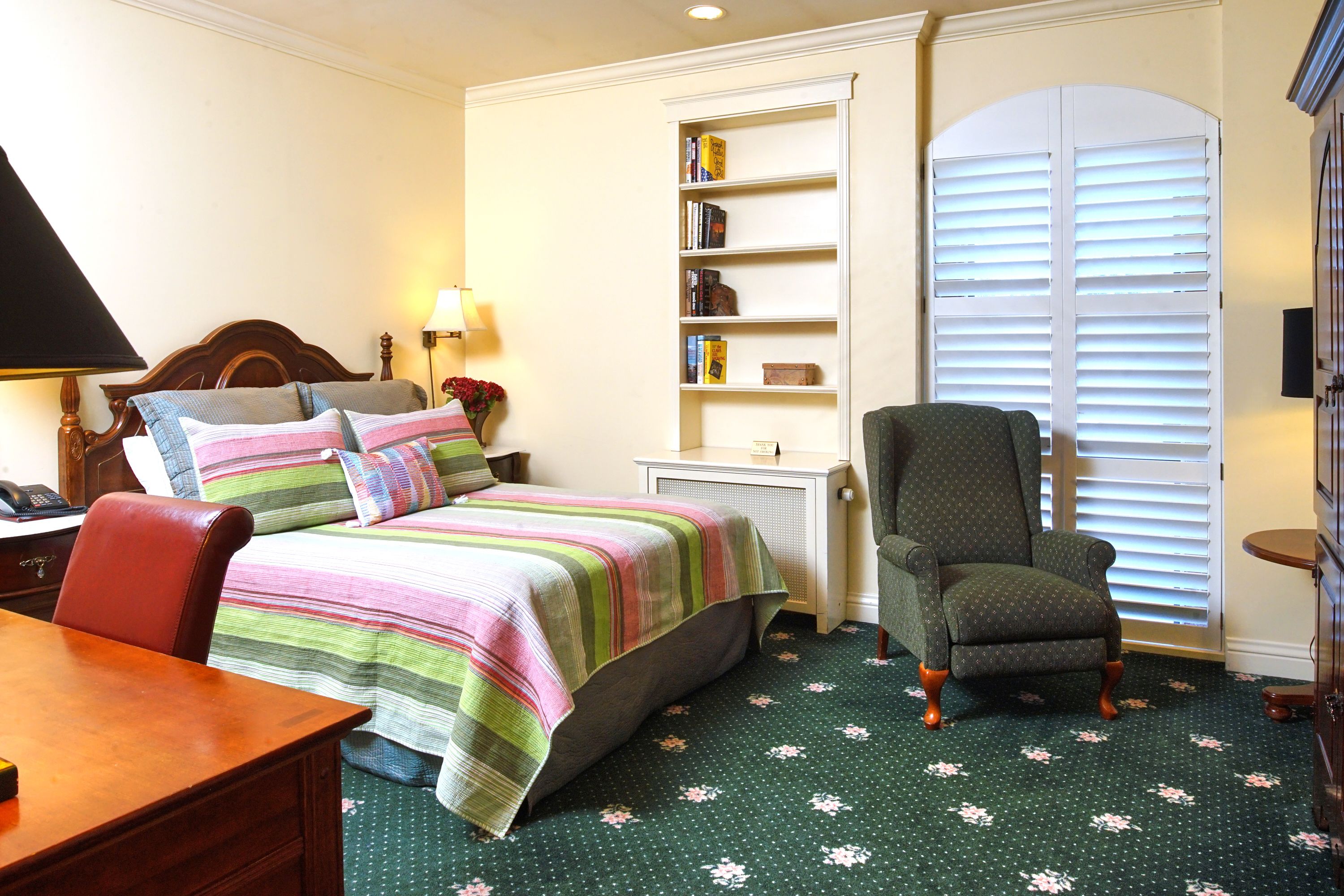 A bedroom with a bed, a chair, a desk, and a bookshelf.