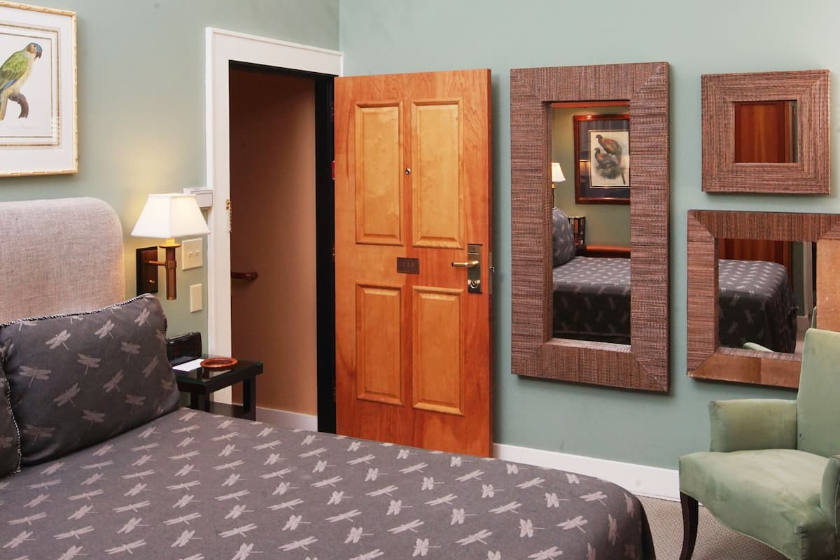 A bedroom with a bed, a chair, a door, and a wall-mounted mirror.