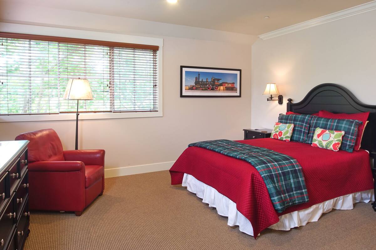A neatly arranged bedroom with a bed, a red chair, a lamp, and a framed picture on the wall.