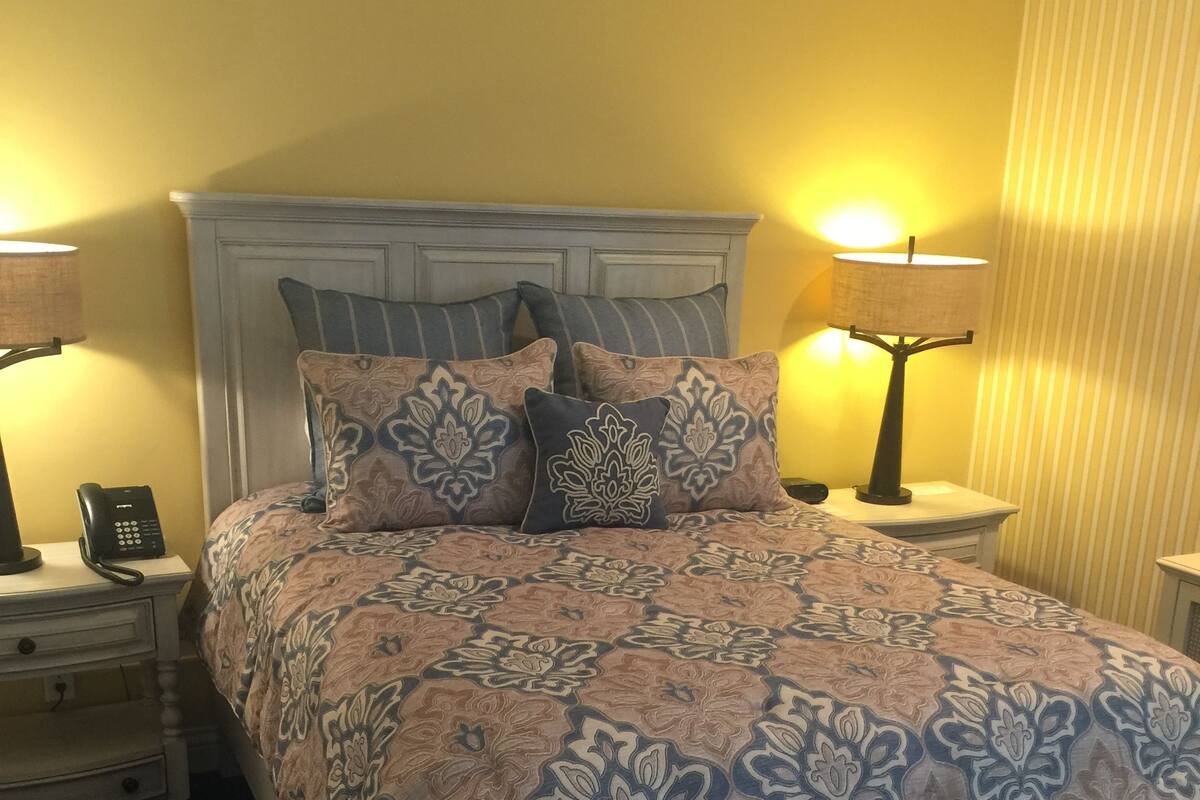 A neatly made bed with patterned bedding, a bedside telephone, and two bedside lamps.