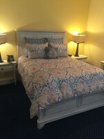 Una cama bien tendida con ropa de cama estampada, un teléfono en la mesita de noche y dos lámparas de noche.