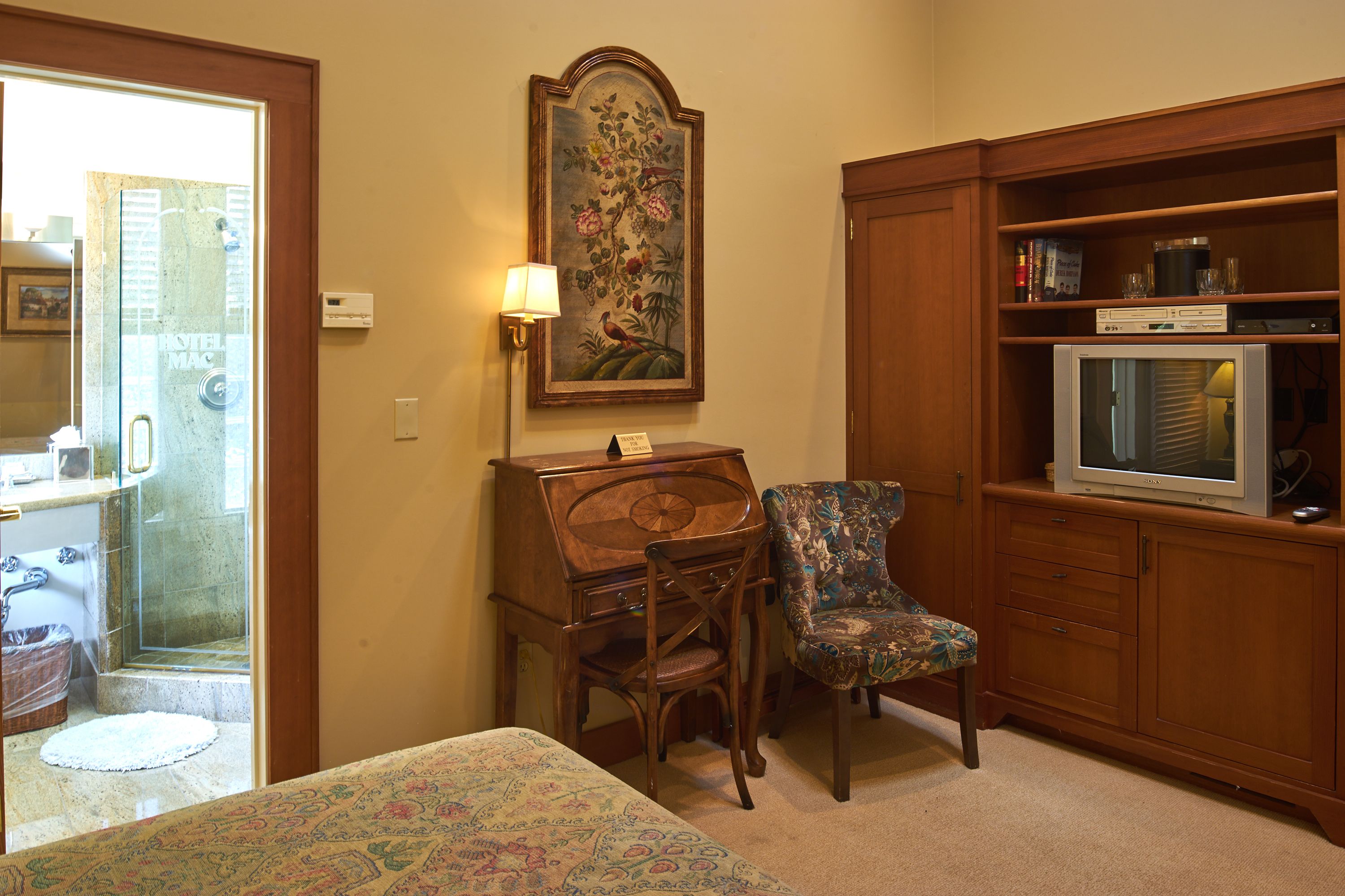 A hotel room with a bed, a desk, a chair, a television, and a painting on the wall.