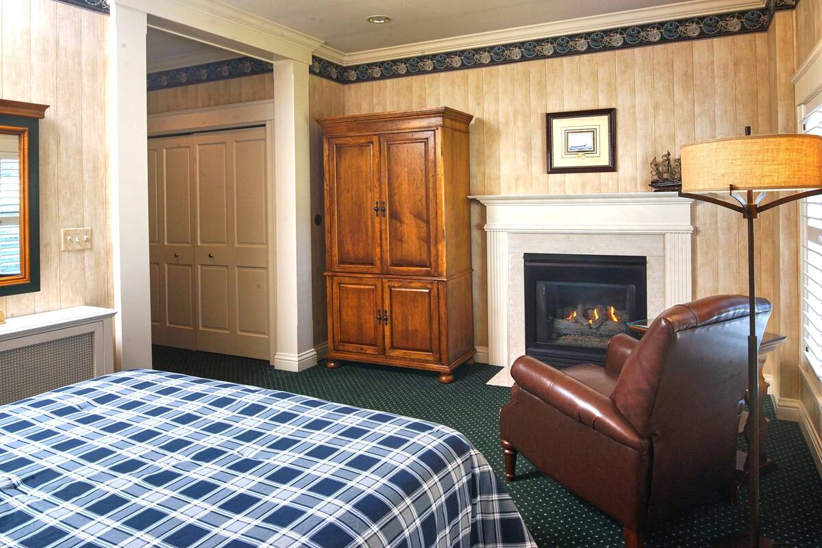 A hotel room with a bed, a fireplace, a leather armchair, and a wardrobe.
