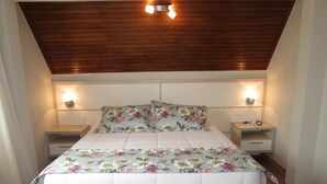 A bedroom with a wooden ceiling, a floral bedspread, two bedside tables, and a nightstand with a lamp. - Olidal Pousada da Serra (Gramado)
