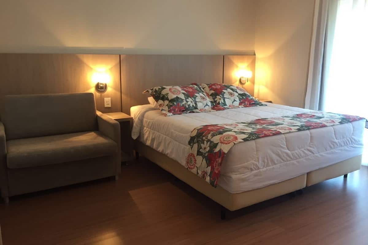 A hotel room with a bed, a sofa, and two wall-mounted lamps.