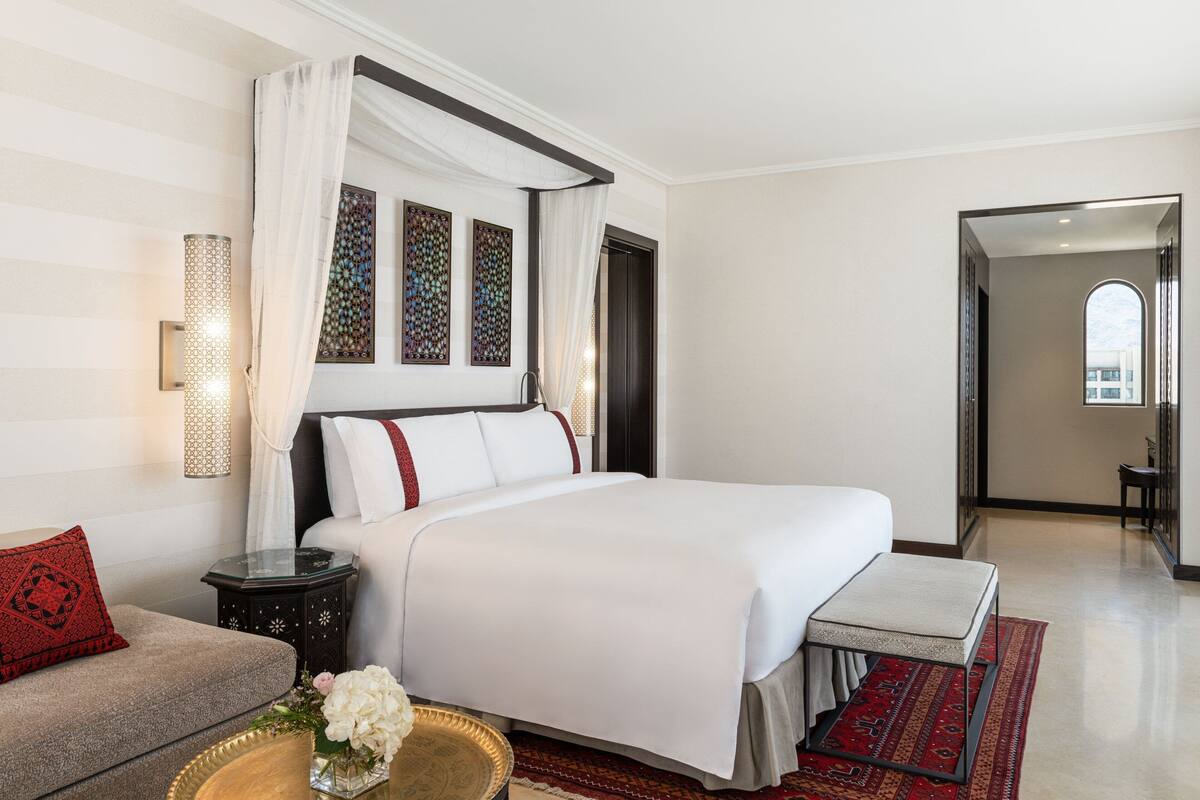 A hotel room with a large bed, a bedside table, a nightstand, a sofa, and a decorative wall piece.