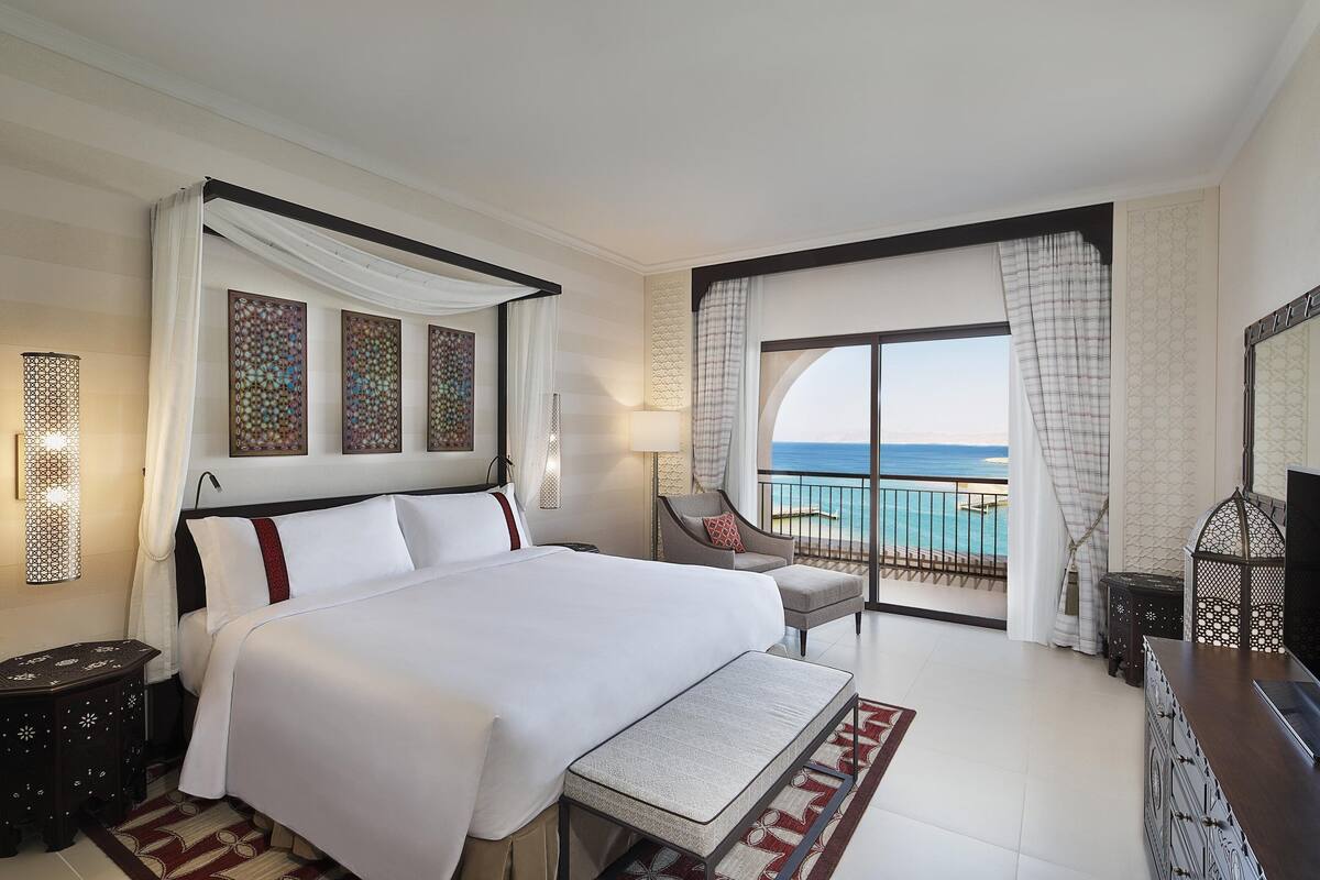 A hotel room with a large bed, a chair, a TV, and a view of the ocean.
