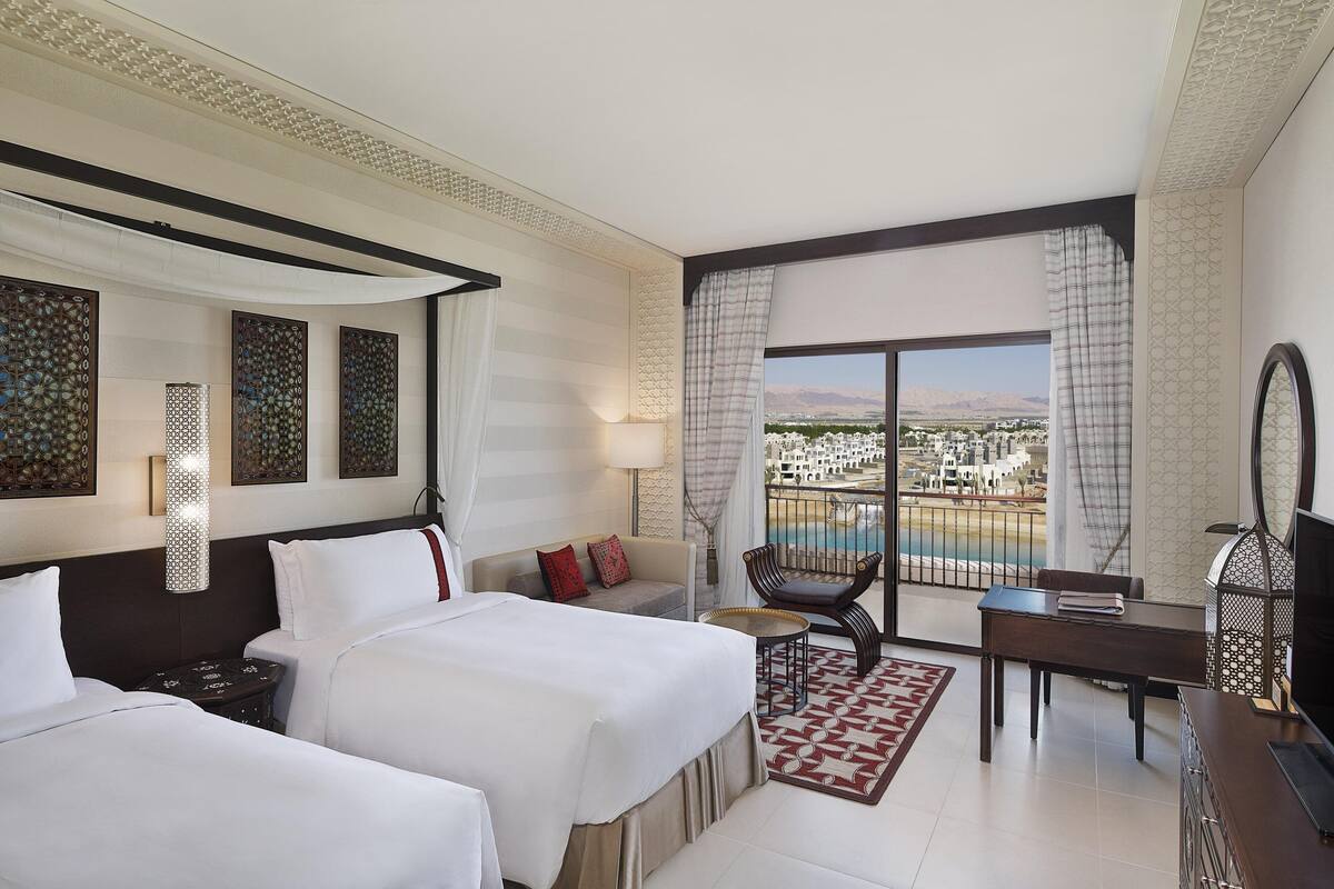 A hotel room with two beds, a balcony with a pool view, a desk, and a TV.