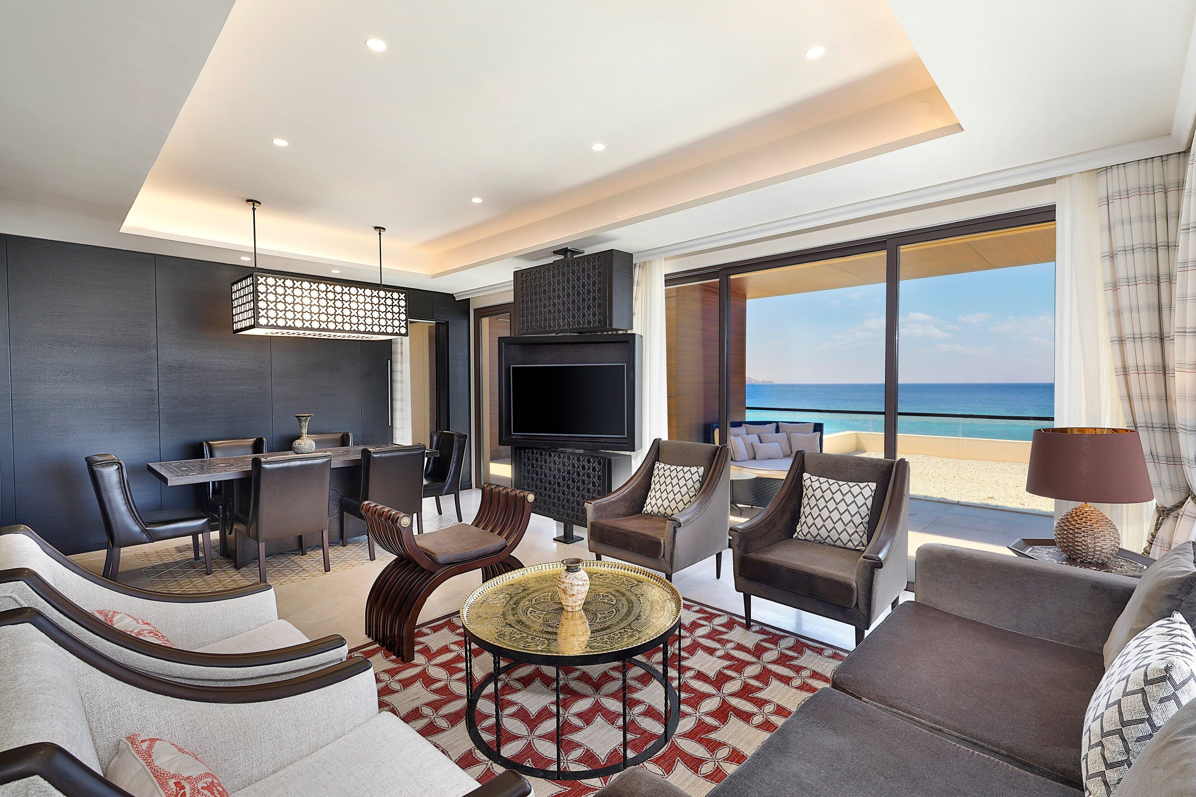 Een moderne woonkamer met een televisie, comfortabele zitplaatsen, een eethoek en een groot raam met uitzicht op het strand.