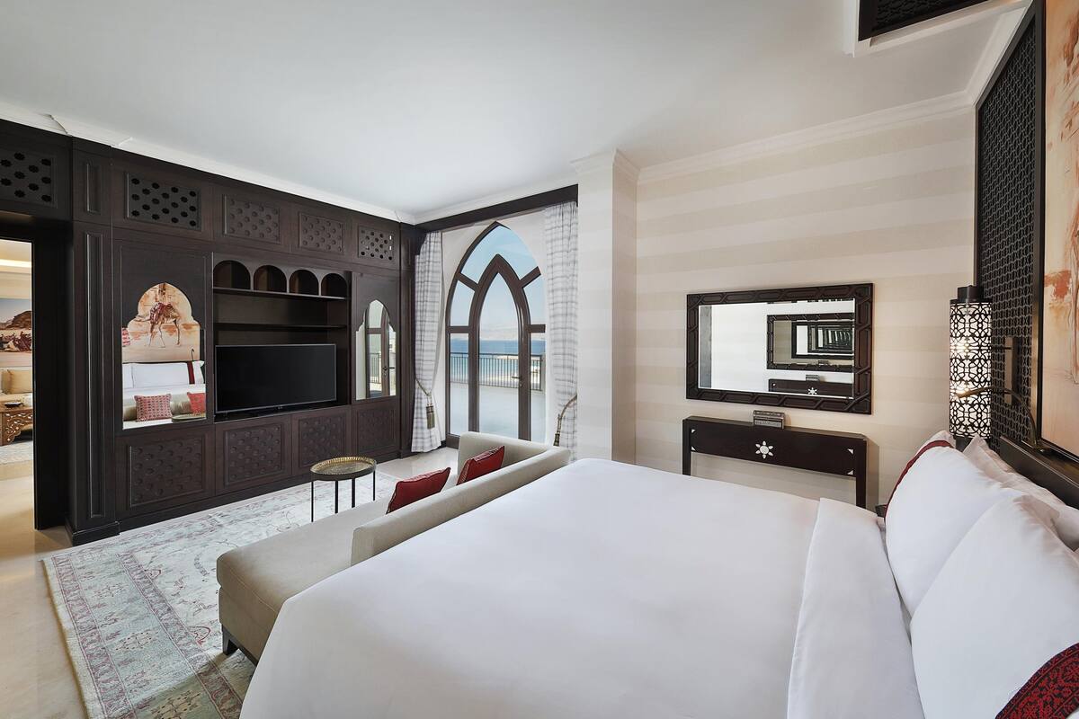 A hotel room with a large bed, a TV, a desk, and a view of the sea.