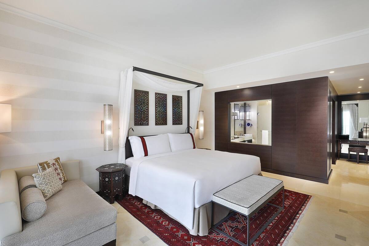 A modern hotel room with a large bed, a sofa, a small table, and a decorative rug.