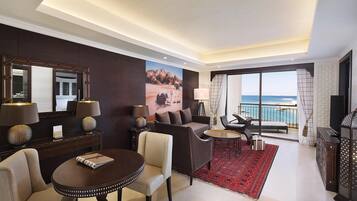 Een moderne hotelkamer met balkon, een bank, een eettafel en een groot raam met uitzicht op zee.