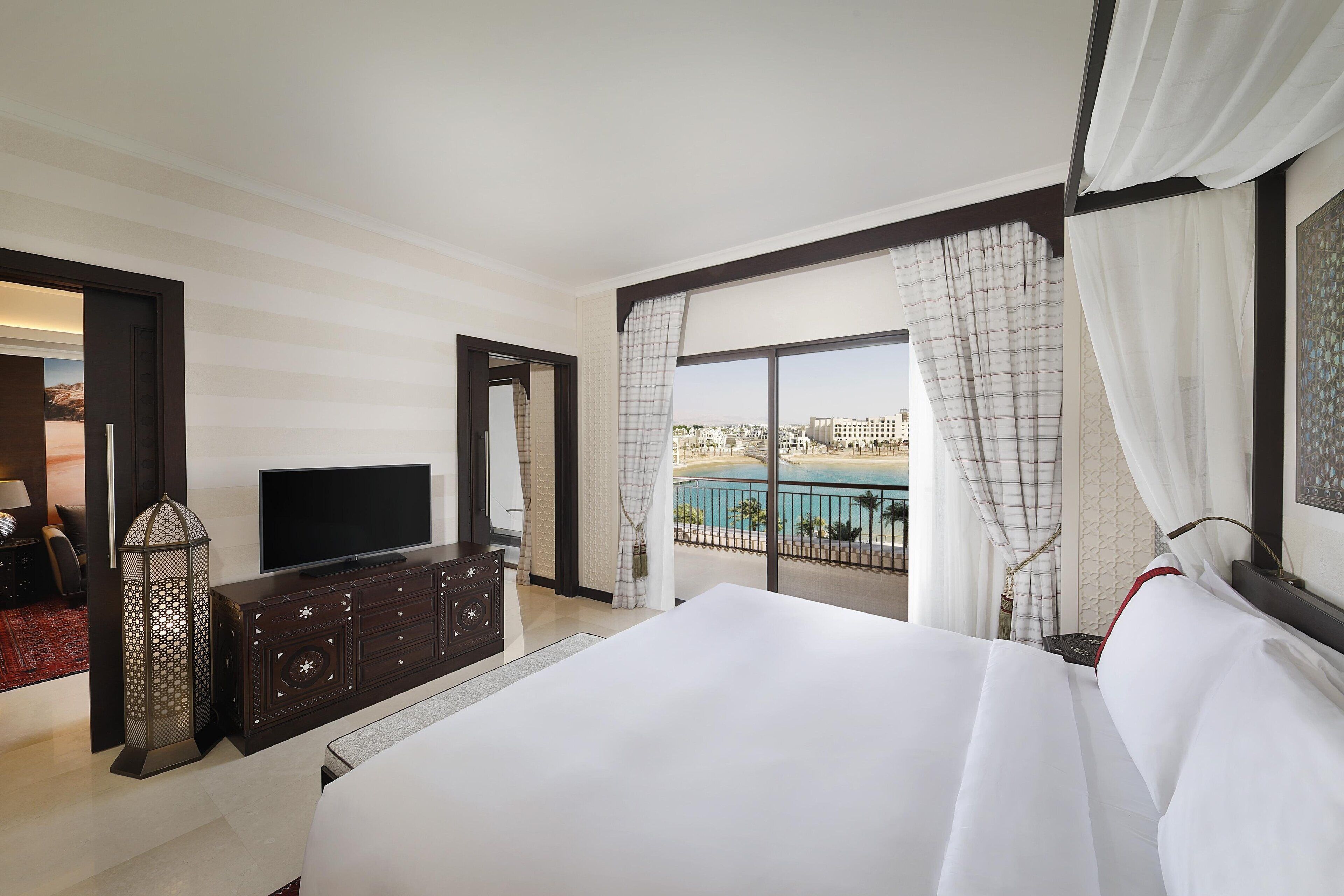 Habitación de hotel con una cama grande, televisión, cómoda y balcón con vista a la piscina.