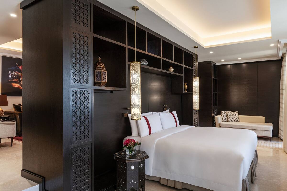 A modern hotel room with a large bed, dark wood paneling, decorative lighting, and a sofa.