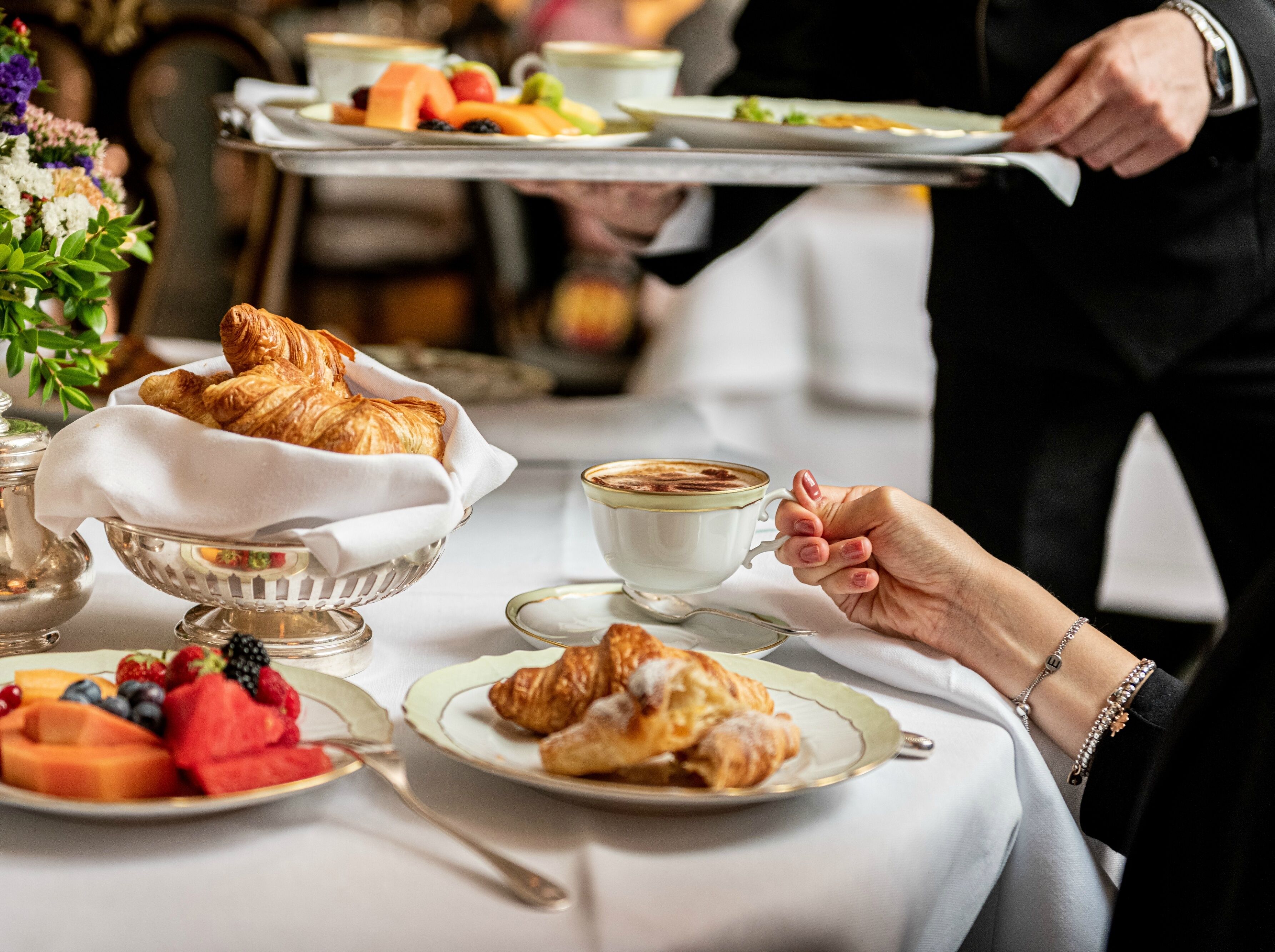 A dining table with croissants, fruit, and a cup of coffee.