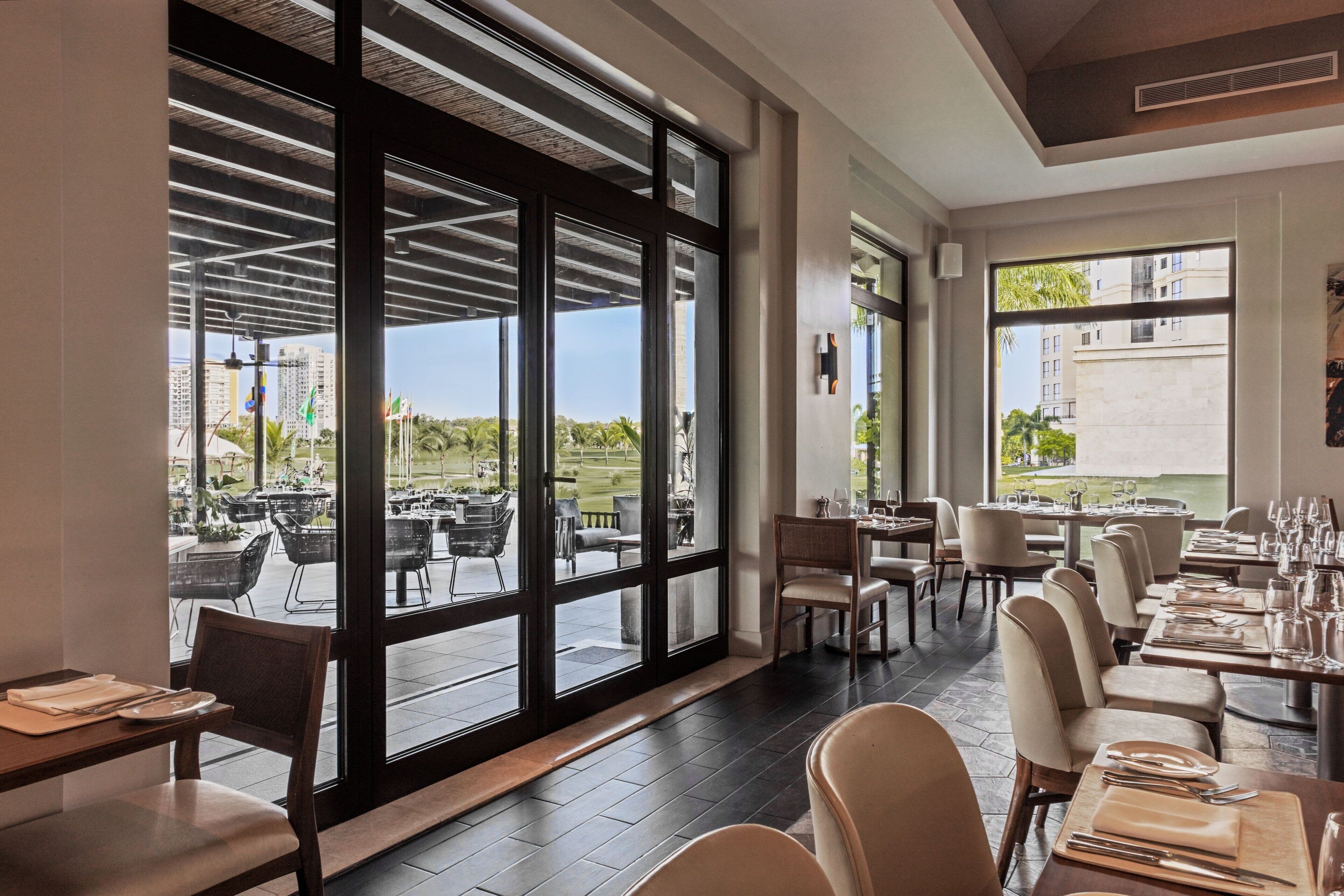 Un restaurant doté de grandes fenêtres, de tables dressées pour le service et offrant une vue sur l’espace extérieur aménagé pour les clients.